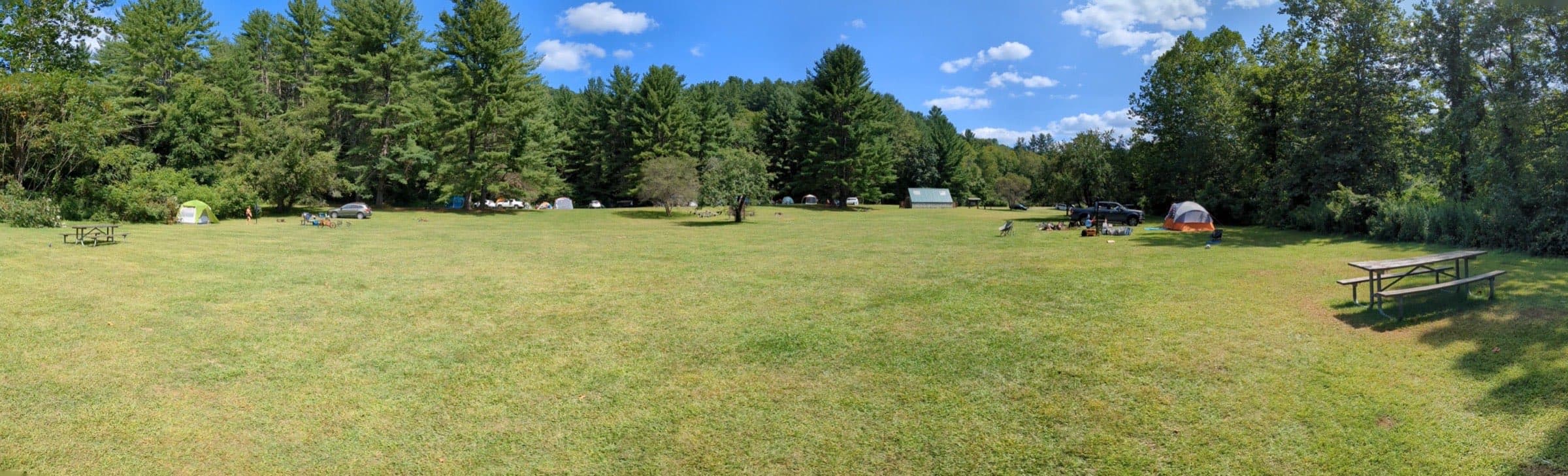 Panorama of the wide open meadow at Indian Hollow, ringed by trees, dotted with family tents